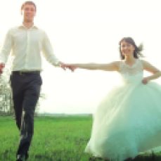 bride and groom running through field